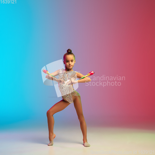 Image of Little caucasian girl, rhytmic gymnast training, performing isolated on gradient blue-red studio background in neon