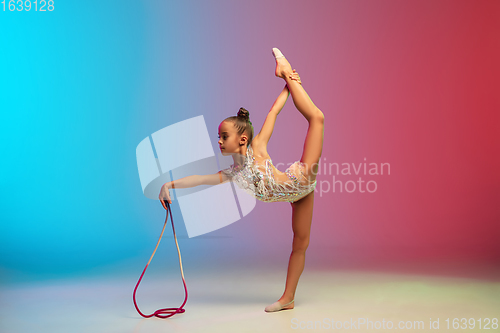 Image of Little caucasian girl, rhytmic gymnast training, performing isolated on gradient blue-red studio background in neon