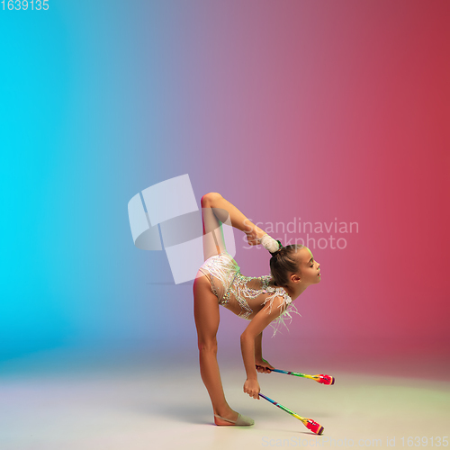 Image of Little caucasian girl, rhytmic gymnast training, performing isolated on gradient blue-red studio background in neon