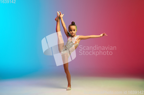 Image of Little caucasian girl, rhytmic gymnast training, performing isolated on gradient blue-red studio background in neon