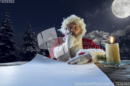 Image of Emotional Santa Claus congratulating with New Year and Christmas, writing a letter, wish list in midnight with candle