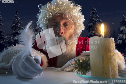 Image of Emotional Santa Claus congratulating with New Year and Christmas, writing a letter, wish list in midnight with candle