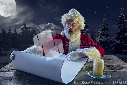 Image of Emotional Santa Claus congratulating with New Year and Christmas, writing a letter, wish list in midnight with candle