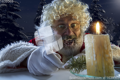 Image of Emotional Santa Claus congratulating with New Year and Christmas, writing a letter, wish list in midnight with candle