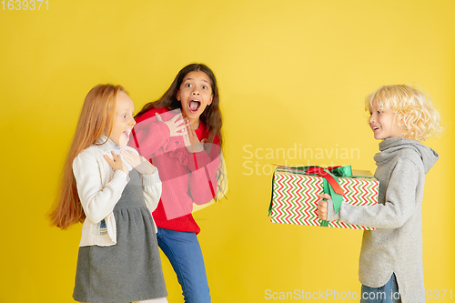 Image of Giving and getting presents on Christmas holidays. Group of happy smiling children having fun isolated on yellow studio background