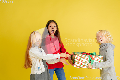 Image of Giving and getting presents on Christmas holidays. Group of happy smiling children having fun isolated on yellow studio background