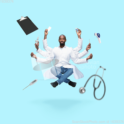 Image of Handsome multi-armed doctor levitating isolated on blue studio background with equipment