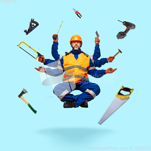 Image of Handsome multi-armed builder levitating isolated on blue studio background with equipment