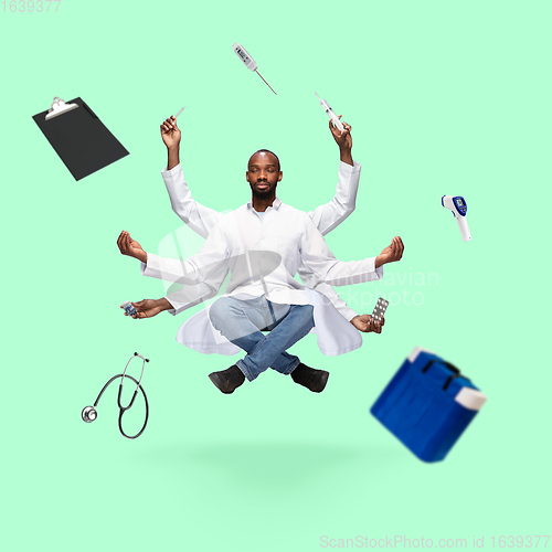 Image of Handsome multi-armed doctor levitating isolated on green studio background with equipment