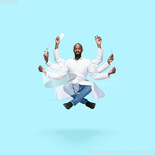 Image of Handsome multi-armed doctor levitating isolated on blue studio background with equipment