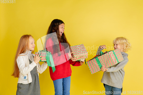 Image of Giving and getting presents on Christmas holidays. Group of happy smiling children having fun isolated on yellow studio background