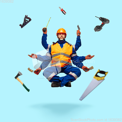 Image of Handsome multi-armed builder levitating isolated on blue studio background with equipment