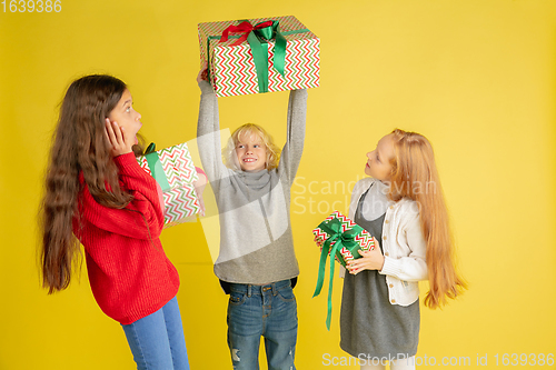 Image of Giving and getting presents on Christmas holidays. Group of happy smiling children having fun isolated on yellow studio background