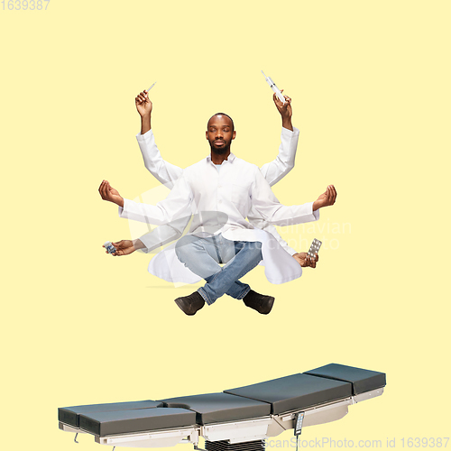 Image of Handsome multi-armed doctor levitating isolated on yellow studio background with equipment