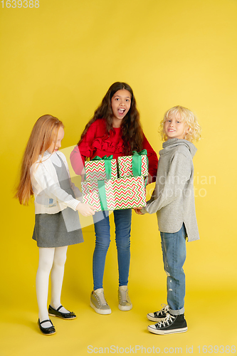 Image of Giving and getting presents on Christmas holidays. Group of happy smiling children having fun isolated on yellow studio background