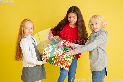 Image of Giving and getting presents on Christmas holidays. Group of happy smiling children having fun isolated on yellow studio background