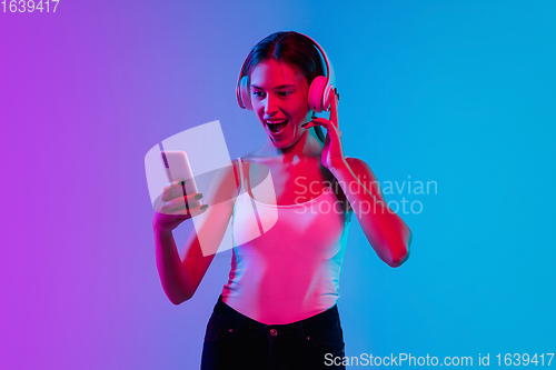 Image of Young caucasian woman\'s portrait on gradient blue-purple studio background in neon light