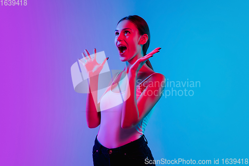 Image of Young caucasian woman\'s portrait on gradient blue-purple studio background in neon light