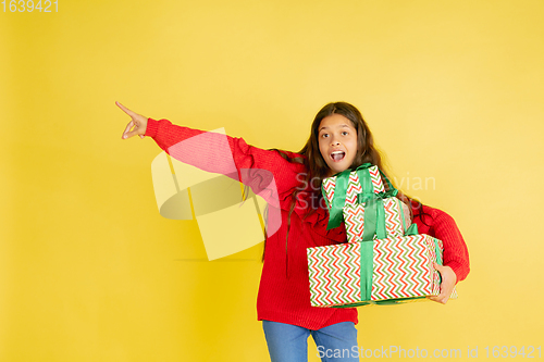 Image of Giving and getting presents on Christmas holidays. Teen girl having fun isolated on yellow studio background