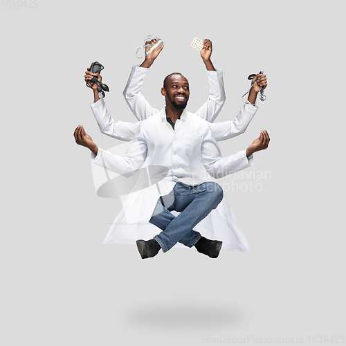Image of Handsome multi-armed doctor levitating isolated on grey studio background with equipment