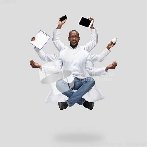 Image of Handsome multi-armed doctor levitating isolated on grey studio background with equipment