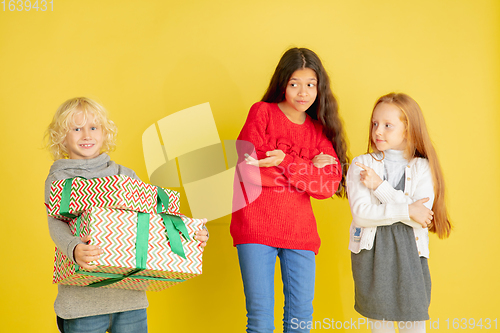 Image of Giving and getting presents on Christmas holidays. Group of happy smiling children having fun isolated on yellow studio background