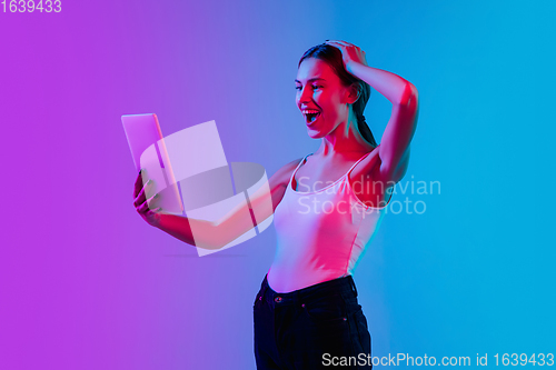 Image of Young caucasian woman\'s portrait on gradient blue-purple studio background in neon light