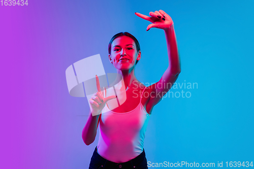 Image of Young caucasian woman\'s portrait on gradient blue-purple studio background in neon light