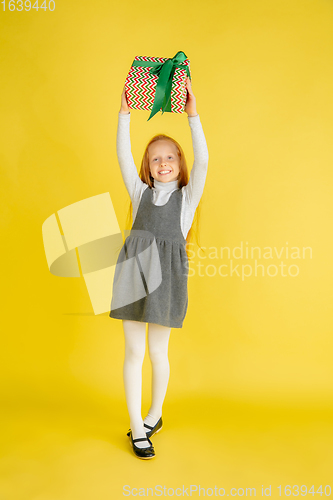 Image of Giving and getting presents on Christmas holidays. Teen girl having fun isolated on yellow studio background