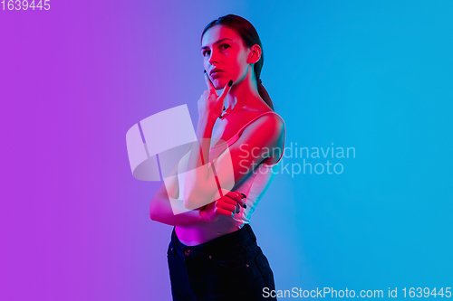 Image of Young caucasian woman\'s portrait on gradient blue-purple studio background in neon light