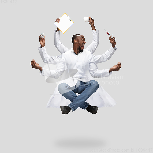 Image of Handsome multi-armed doctor levitating isolated on grey studio background with equipment