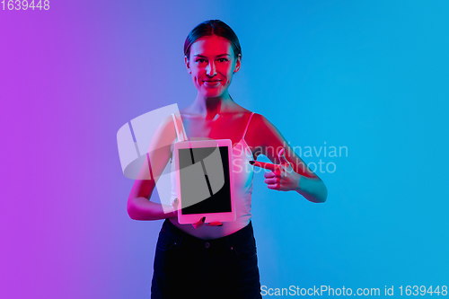 Image of Young caucasian woman\'s portrait on gradient blue-purple studio background in neon light