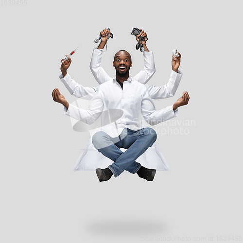 Image of Handsome multi-armed doctor levitating isolated on grey studio background with equipment