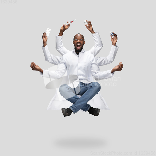 Image of Handsome multi-armed doctor levitating isolated on grey studio background with equipment