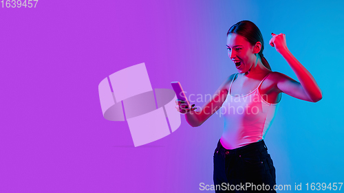 Image of Young caucasian woman\'s portrait on gradient blue-purple studio background in neon light