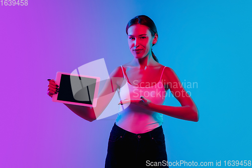 Image of Young caucasian woman\'s portrait on gradient blue-purple studio background in neon light