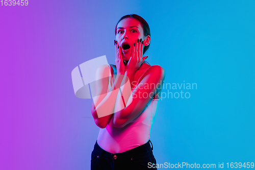 Image of Young caucasian woman\'s portrait on gradient blue-purple studio background in neon light