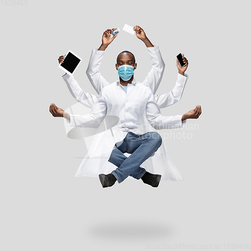 Image of Handsome multi-armed doctor levitating isolated on grey studio background with equipment