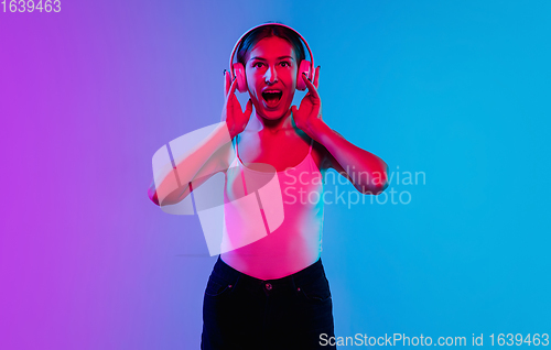 Image of Young caucasian woman\'s portrait on gradient blue-purple studio background in neon light