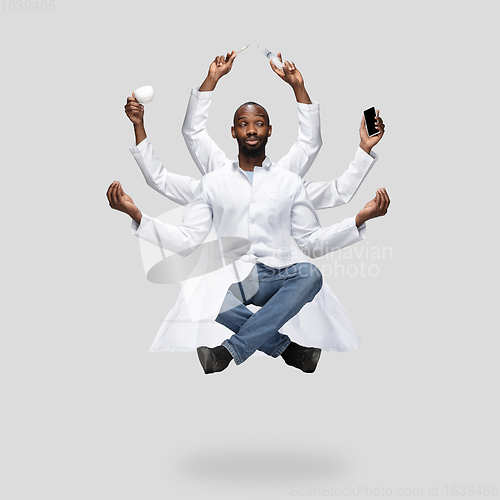 Image of Handsome multi-armed doctor levitating isolated on grey studio background with equipment