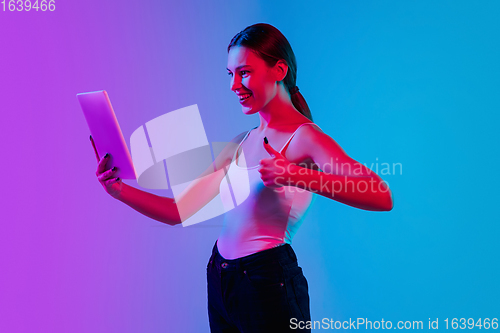 Image of Young caucasian woman\'s portrait on gradient blue-purple studio background in neon light