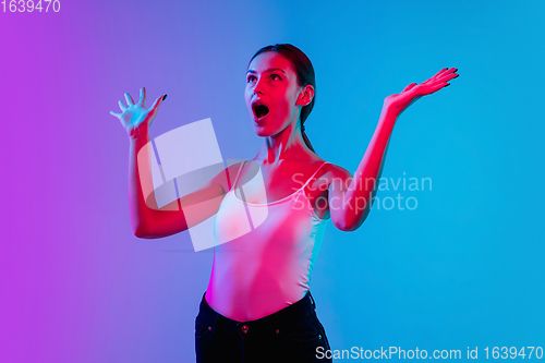 Image of Young caucasian woman\'s portrait on gradient blue-purple studio background in neon light