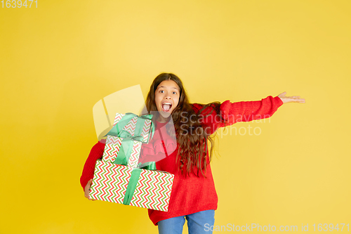 Image of Giving and getting presents on Christmas holidays. Teen girl having fun isolated on yellow studio background