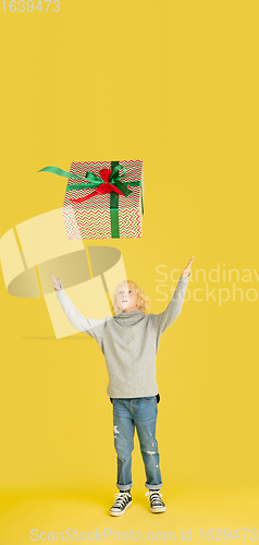 Image of Giving and getting presents on Christmas holidays. Little boy having fun isolated on yellow studio background