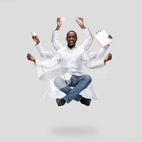 Image of Handsome multi-armed doctor levitating isolated on grey studio background with equipment