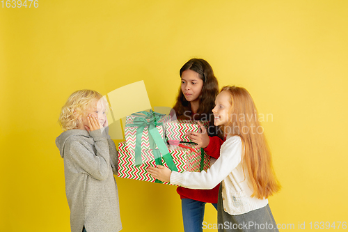 Image of Giving and getting presents on Christmas holidays. Group of happy smiling children having fun isolated on yellow studio background