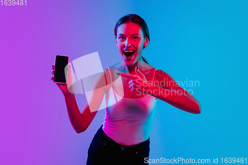 Image of Young caucasian woman\'s portrait on gradient blue-purple studio background in neon light