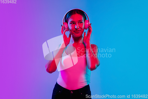Image of Young caucasian woman\'s portrait on gradient blue-purple studio background in neon light
