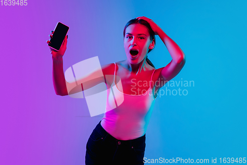 Image of Young caucasian woman\'s portrait on gradient blue-purple studio background in neon light