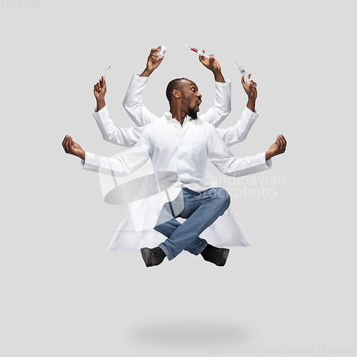 Image of Handsome multi-armed doctor levitating isolated on grey studio background with equipment